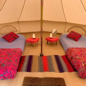 a room with two beds and two tables in a tent at Fred's Yurts at Hay Festival in Hay-on-Wye