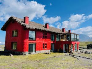 ein rotes Haus mit einem Strohdach auf einem Feld in der Unterkunft Hotel Tambopaxi in Machachi