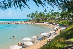 ein Strand mit Sonnenschirmen und Menschen im Wasser in der Unterkunft Nannai Residence Frente Piscina Muro Alto Beira Mar in Porto De Galinhas