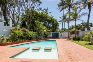 una piscina con 2 bancos en un patio trasero con palmeras en Chaka's Cove, en Ballito