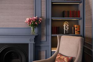 a room with a fireplace and a chair with a vase of flowers at The Tophams Hotel in London