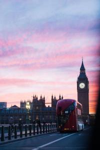 a double decker bus driving down a street with a clock tower at The Tophams Hotel in London