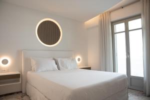 a white bedroom with a large bed and a mirror at Tzanis Resort Skyros in Skiros