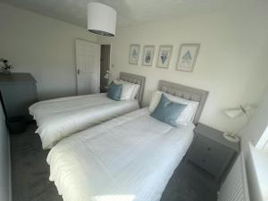 two beds in a bedroom with white sheets and blue pillows at Alma Court Retreat Freshwater IOW in Freshwater