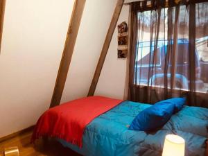 Una cama con una manta roja y azul y una ventana en Refugio del Pollux- Coyhaique- Orillas Lago Pollux, en Coyhaique