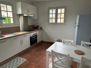 a kitchen with white cabinets and a white table and a table and a refrigerator at Chez Alice - Isigny le Buat in Isigny-le-Buat