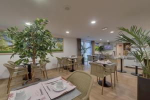 a restaurant with tables and chairs and potted plants at Hotel The Originals Bernay Acropole in Bernay