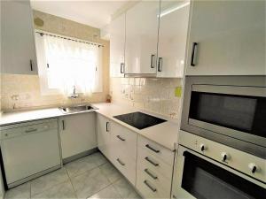 cocina con armarios blancos, fregadero y microondas en Villa Service - Prat de Calafell, en Calafell