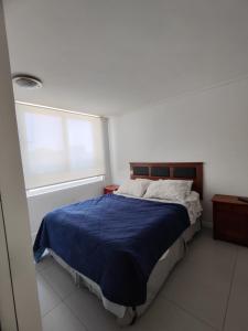 a bedroom with a bed with a blue comforter and a window at Sector Av. Brasil 1D1B - 4P edificio in Antofagasta