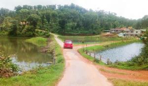 a red car driving down a dirt road next to a lake at Hiddenvalley Stays - Riverside in Madikeri