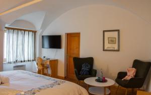 a bedroom with a bed and chairs and a tv at Hotel Corona in Vicosoprano