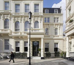 a woman walking in front of a large building at Signature Townhouse London Hyde Park in London