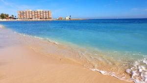 una spiaggia con l'oceano e un edificio sullo sfondo di Casa Del Angel , Cosy 2 bed apartment,150m from Playa Los Locos plus beautiful swimming pool a Torrevieja