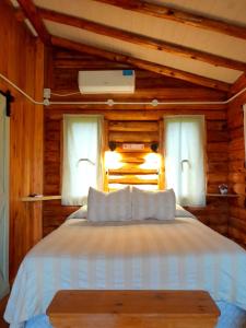 um quarto com uma cama com lençóis brancos e 2 janelas em Cabaña Rural El Encuentro em San Antonio de Areco