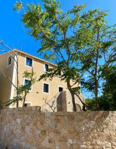 a building behind a stone wall with a tree at Casa u fornu Residence & Spa in LʼÎle-Rousse
