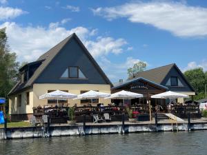 un restaurant avec des tables et des parasols à côté d'une rivière dans l'établissement Ausflugsrestaurant & Pension Aalbude & Hausfloßvermietung am Kummerower See, à Dargun