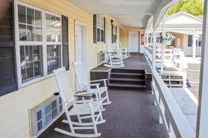 a row of white chairs on the porch of a building at Longhouse Lodge Motel in Watkins Glen