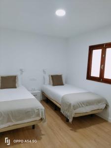 Habitación con 2 camas, paredes blancas y suelo de madera. en Texeda Room Suites en Tejeda