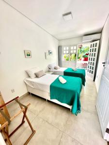 a bedroom with two beds with green sheets and a chair at Vista para o mar Arraial d'Ajuda in Arraial d'Ajuda