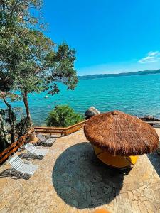 a straw umbrella and chairs next to the water at Casa pé na areia para até 14 pessoas em bombinhas in Bombinhas