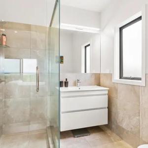 baño blanco con ducha y lavamanos en Coastal Paradise, en Raglan