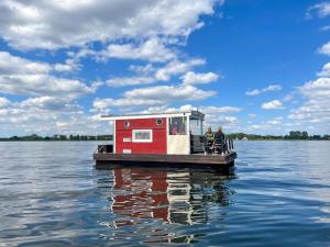 DargunHausfloßvermietung auf der Peene am Kummerower See in Mecklenburg Vorpommern 15 PS的一艘在水面上装着红色房子的小船