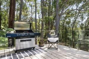 a grill and a chair on a deck with trees at Luxury at MacMasters Beach in Macmasters Beach