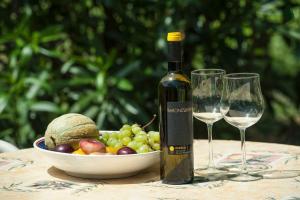 アチレアーレにあるCome In Sicily La Pietra Monacaのワイン1本、テーブル上のグラス2杯(フルーツボウル付)