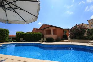 a swimming pool with an umbrella next to a house at Apartments Meri in Ližnjan