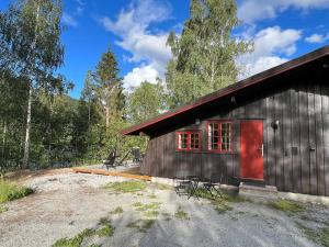 a small cabin with a red door in the woods at Koselig hytte med uteplas ved Hallingdalselva in Al