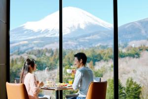 Fuji Speedway Hotel - The Unbound Collection by Hyatt في Oyama: جلوس رجل وامرأة على طاولة مطلة على جبل