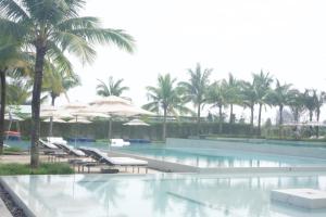 a pool with chairs and umbrellas and palm trees at Sunshine Apartment in 5* resort in Da Nang