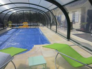 a swimming pool in a greenhouse with green chairs at L'Anctovillière in Anctoville