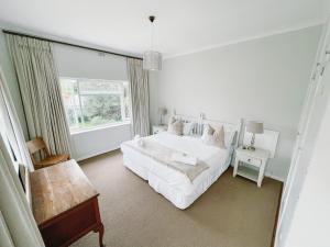 a white bedroom with a bed and a window at Leisure Isle Seaside Cottage in Knysna