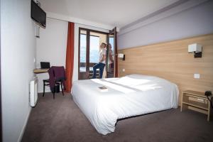 a hotel room with a bed and a woman looking out the window at Villages Clubs du Soleil - LES MENUIRES in Les Menuires