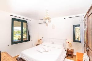 a white bedroom with a bed and two windows at Villa Biderrosa in Orosei