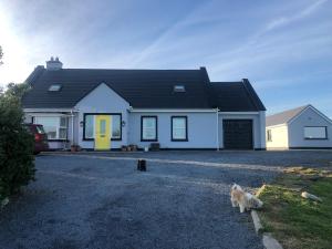 a white house with a dog sitting in the driveway at Cois na Mara Eire code V15 T677 in Bridge of Ross