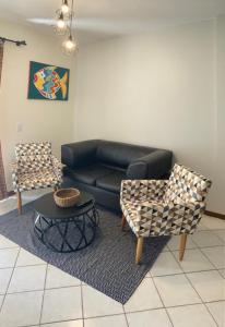 sala de estar con sofá de cuero negro y 2 sillas en Hermoso departamento en Bombas con vista al mar, en Bombinhas