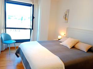 1 dormitorio con 1 cama grande con silla azul y ventana en Portbeach, en Viveiro