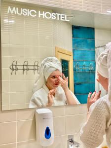 een vrouw met een handdoek op haar hoofd die in een badkamerspiegel kijkt bij Music Hostel in Poltava