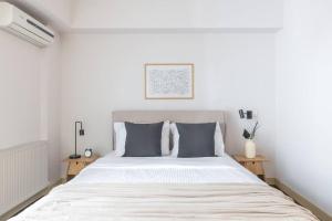 een witte slaapkamer met een groot bed met grijze kussens bij Panoramic 1BR Apartment near Kallimarmaro Stadium by UPSTREET in Athene