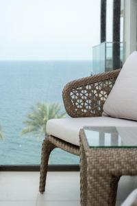una silla de mimbre y una mesa de cristal frente a una ventana en Alnoon at Address Beach Resort Fujairah, en Sharm