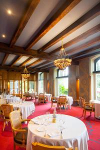 un comedor con mesas y sillas blancas y ventanas en Hôtel & Spa de La Bretesche, en Missillac