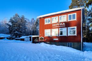 Ein rotes Gebäude mit einem Schild im Schnee. in der Unterkunft Hovra Vandrarhem in Korskrogen