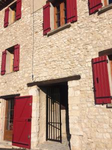 een stenen gebouw met rode deuren en ramen bij LA MAISON D’ALICE in Sault-de-Vaucluse