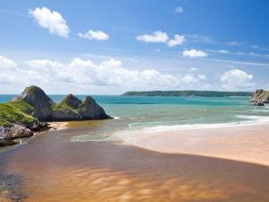 a beach with rocks in the water and the ocean at Cilhendre Holiday Cottages - The Old Cowshed in Swansea