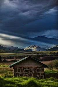 an old building in the middle of a field with mountains at The Stone Barn in Underberg