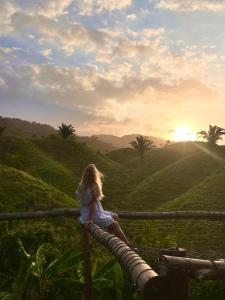 Uma menina sentada numa cerca a ver o pôr-do-sol. em The Valley Tayrona hostel- A unique social jungle hostel em El Zaino