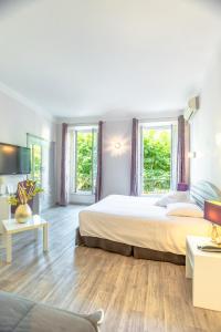 a bedroom with a large bed and two windows at Hotel Les Palmiers in Sainte-Maxime