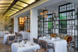 a restaurant with white tables and chairs and windows at Ciêla, Lusaka, a Tribute Portfolio Resort and Spa in Lusaka